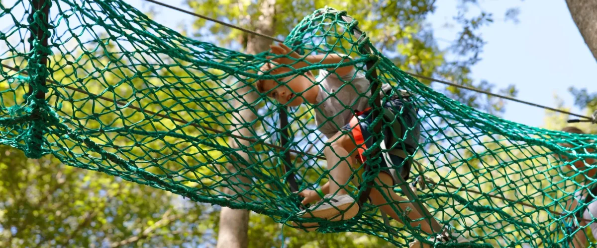 Un garçon en train de faire un parcours aventure dans un filet dans les arbres