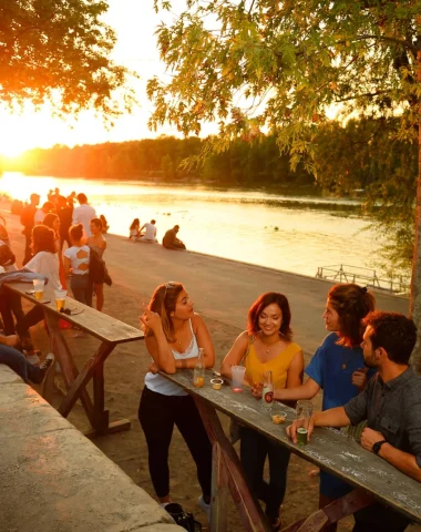 Sur les bords de Loire, en soirée, des groupes de jeunes gens attablés et qui se désaltèrent